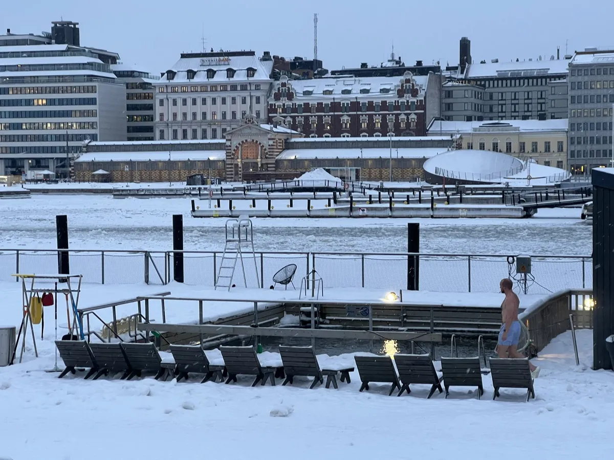 雪の舞う中、桟橋の屋外プール脇を歩く水着の男性