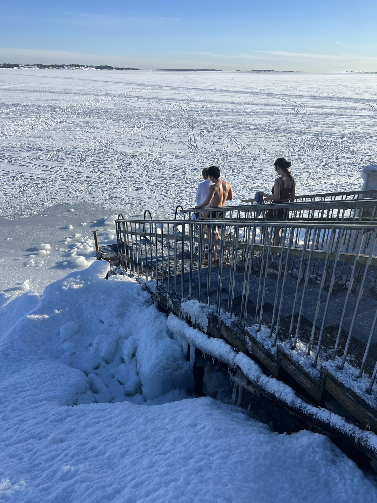 氷結した海の氷穴デッキで涼む水着姿の人たち